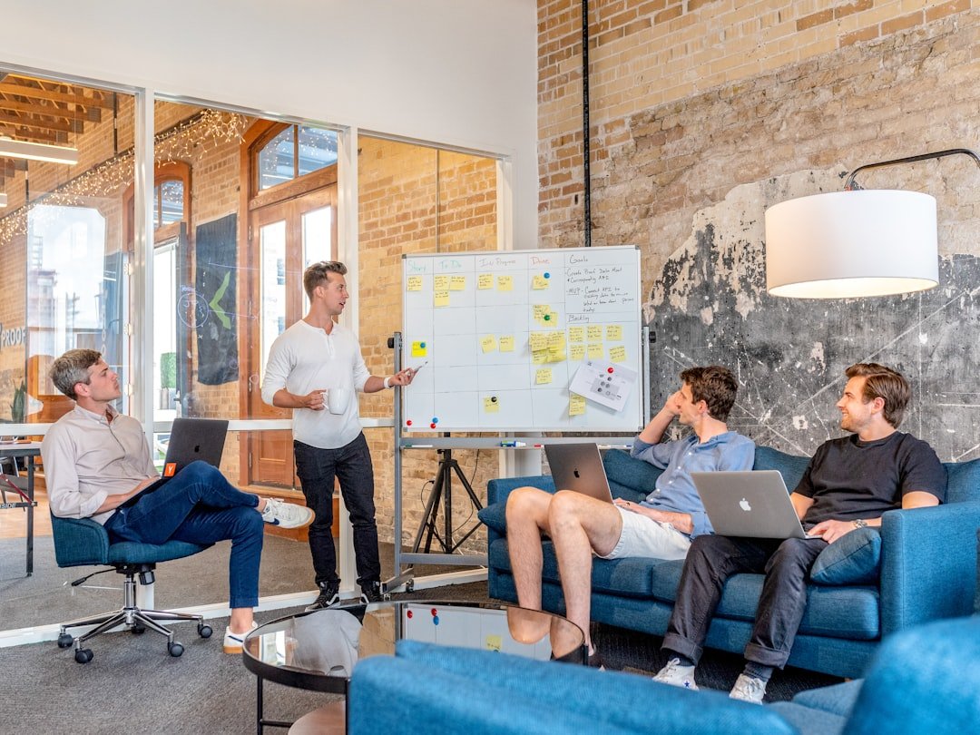 Startup founders reviewing strategy at a whiteboard with teammates on laptops