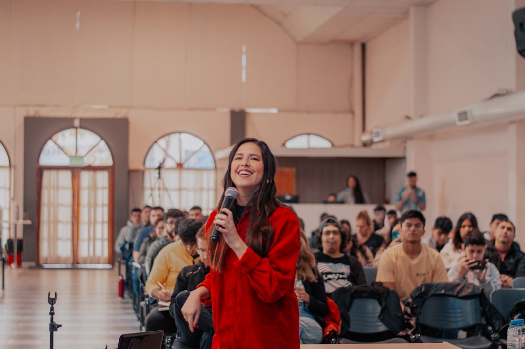 A speaker laughing while holding a microphone in front of a seated audience, demonstrating how to make a presentation funny