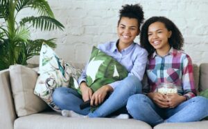 Two friends laughing on a couch with popcorn and a remote, the relaxed mood of a PowerPoint night at home