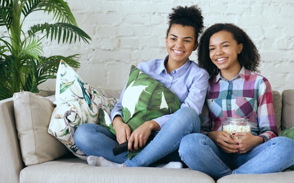 Two friends laughing on a couch with popcorn and a remote, the relaxed mood of a PowerPoint night at home